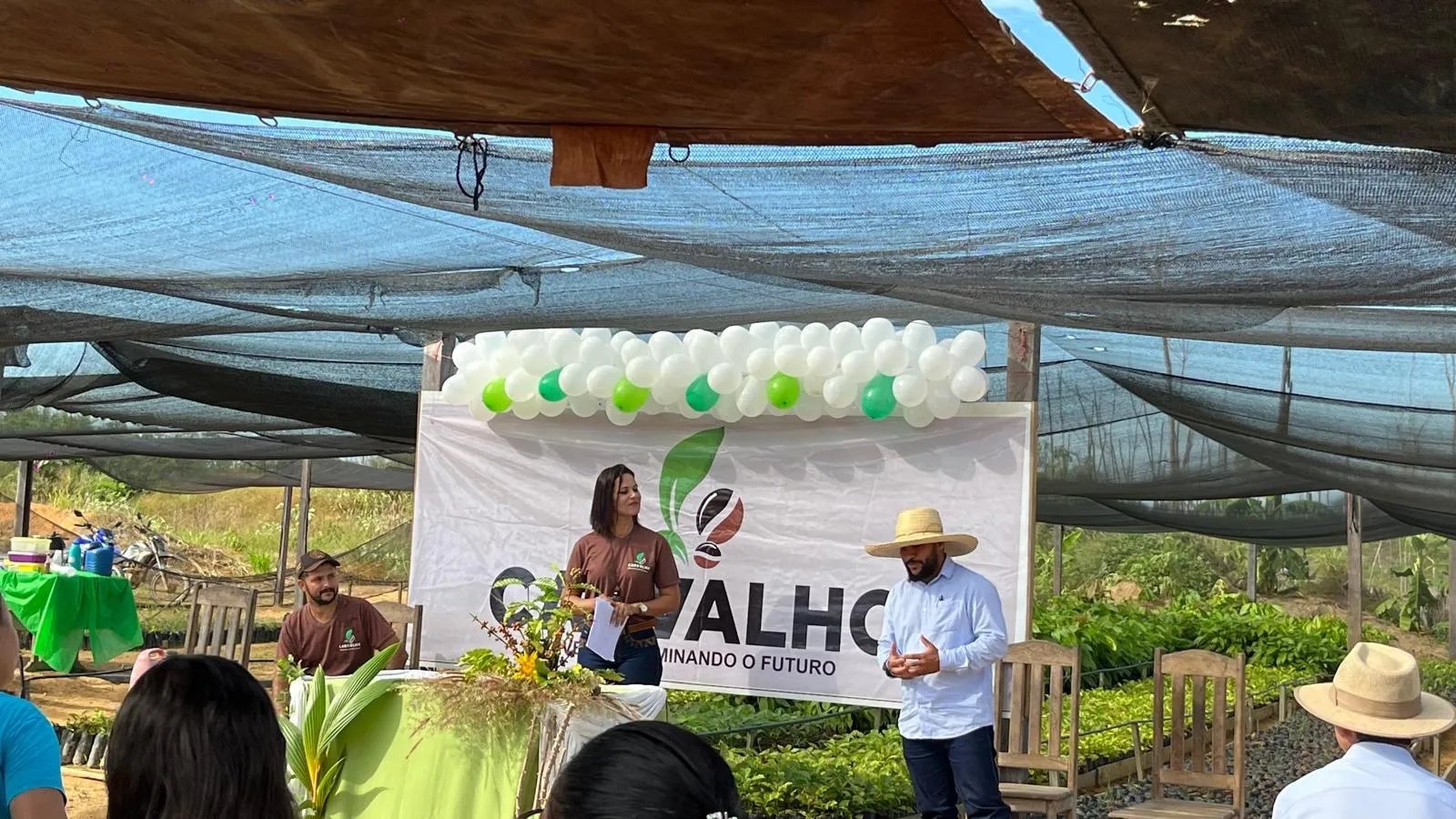 A member addressing an audience beneath the Carvalho banner decorated with balloons, at the nursery.