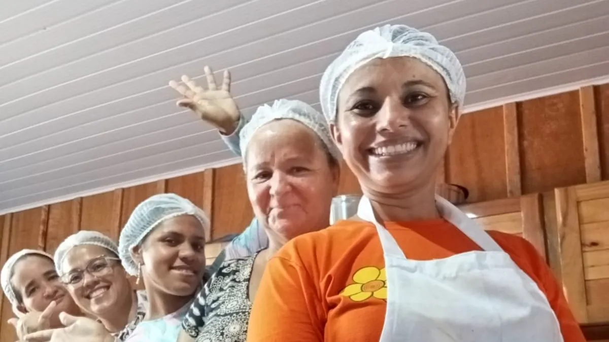Five women members in hairnets and white aprons lined up inside the processing building, smiling at the camera.