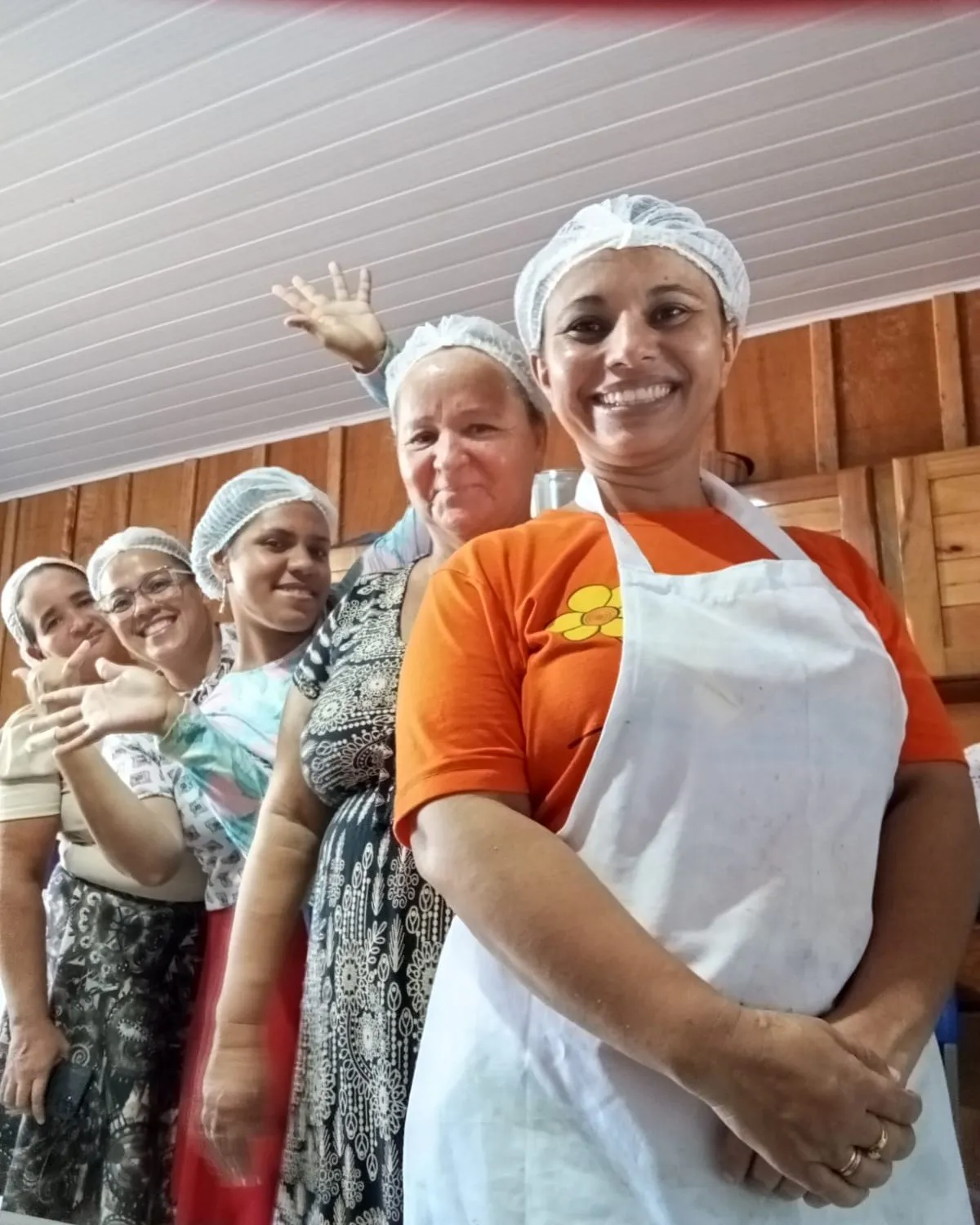 Five women in hairnets and white aprons lined up inside the processing building, smiling at the camera.