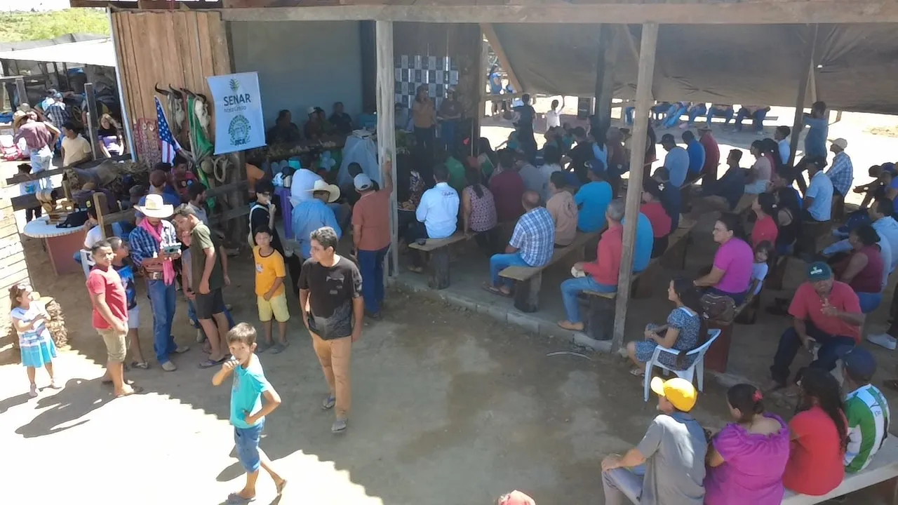 Visitors seated on benches and standing under an open-sided shed during the field day, with a SENAR banner behind them.