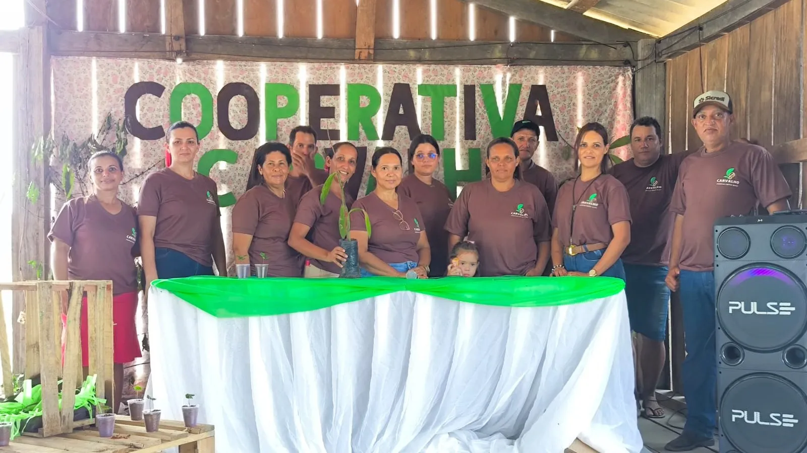 The cooperative team lined up on the wooden stage, beneath the "Cooperativa Carvalho" sign.