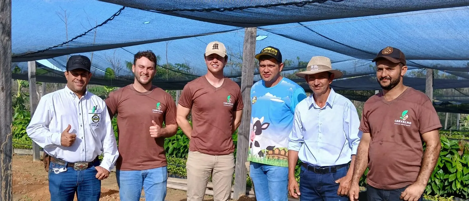 Six men standing under the nursery shade cloth, several wearing Carvalho and partner-institution shirts.