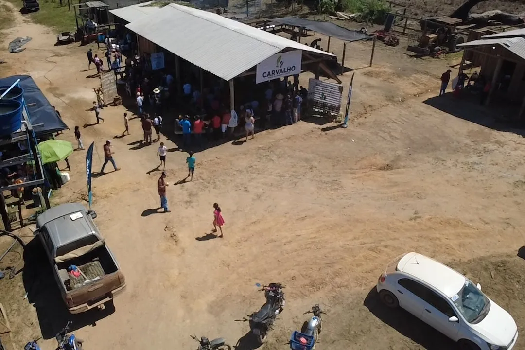 Aerial view of a shed with a Carvalho banner, people gathered around it and cars parked on the bare ground.