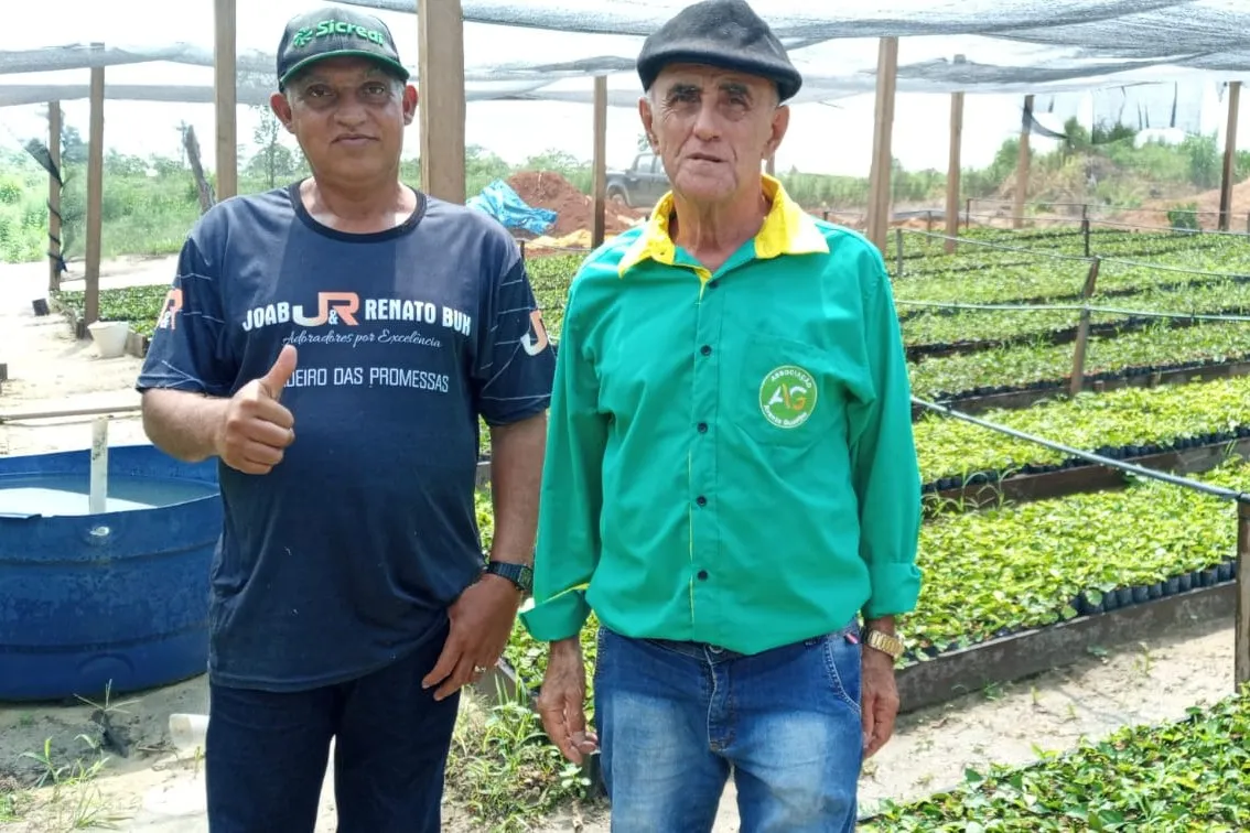 Two members standing in the nursery beside raised beds of seedling trays.